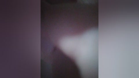 A blurry, dimly-lit video shows a person's upper torso, likely male, with a visible nipple and undefined genital area. The background is dark, making the subject's skin appear pale and indistinct.