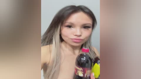 Video of a topless young woman with long, dark hair and light skin, holding a bottle of Pepsi. She has a neutral expression.