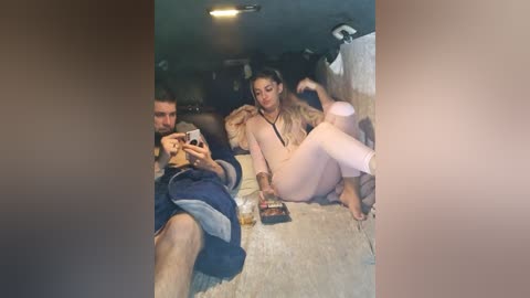 Video of a man and woman, both nude, lounging on a carpeted floor with dim lighting, blurred background, and visible tattoos.