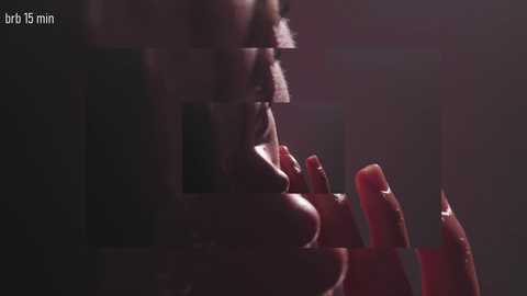Video of a close-up, dimly lit scene featuring a partially blurred hand with manicured nails, fingers gently touching a red object. The background is dark and indistinct, emphasizing the focus on the hand and object.