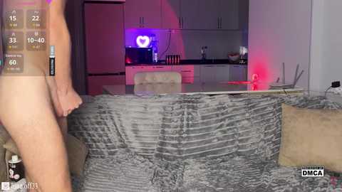 A video of a nude man standing in a dimly lit modern kitchen with gray textured wallpaper, white cabinets, and a heart-shaped neon light.