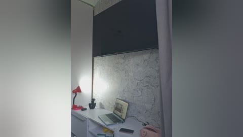 Video of a small, minimalist room with a concrete wall, a black TV, a red lamp, a laptop, and a pink object on a white shelf.