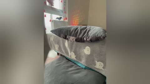 Video of a bed with a grey, patterned duvet and matching pillow, partially obscured by a white curtain. The room has a beige wall and a red, star-shaped light fixture.
