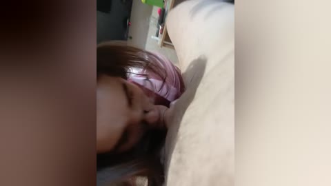 Video of a woman with light skin and pink hair, performing oral sex on a man with a light-skinned torso. The background features a blurred indoor setting.