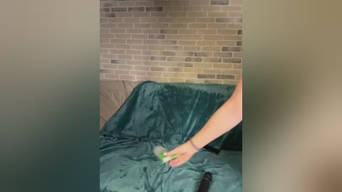 A video of a person in a teal velvet robe, standing in a room with a brick wall backdrop. The person is holding a green object, possibly a remote control, and the room appears cozy and well-lit.