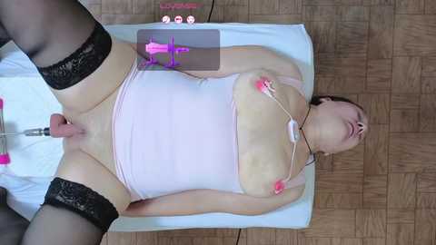 A video shows a nude woman with fair skin, wearing black thigh-high stockings, lying on a wooden floor. She's engaged in sexual activity with a pink vibrator, her legs spread wide.