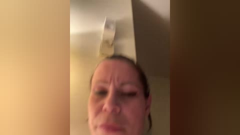 A blurred, close-up video of a Caucasian woman with light skin, short brown hair, and a neutral expression, taken indoors with soft lighting.