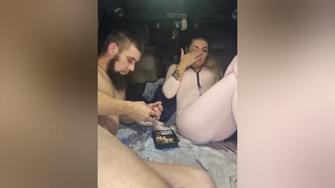 Video of a nude man and a woman in matching pink pajamas, engaging in oral sex on a bed, blurred background.