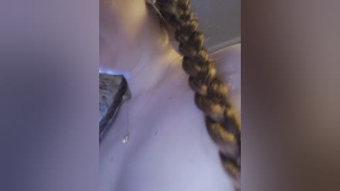 A video captures a close-up of a woman with a thick, curly brown braid, partially obscured by a white bathroom faucet.