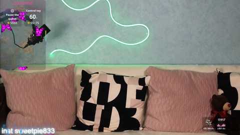 Video of a modern living room with a pink couch, black-and-white patterned pillows, and a glowing green neon wall art.