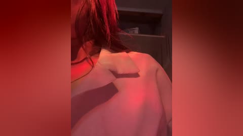 Video of a nude person with fair skin, shoulder-length red hair, and visible tattoos on the back, illuminated by red light.