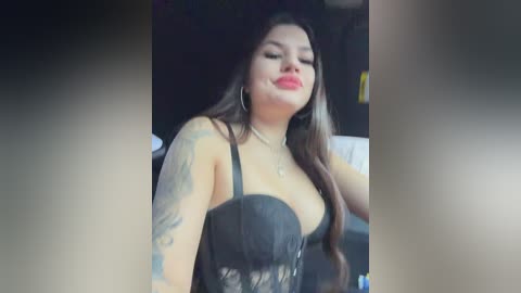 Video of a young woman with long, dark hair, fair skin, and tattoos on her arms, wearing a black lace top, smiling, with a blurred background.