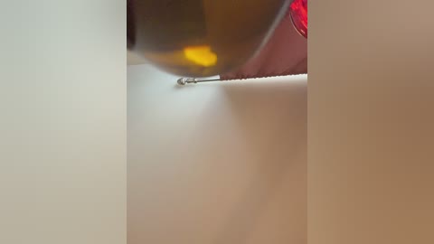 A video of a close-up, blurry scene showing a person with a red shirt, holding a bottle of brown liquid, about to pour it onto a white surface, creating a small, circular puddle.