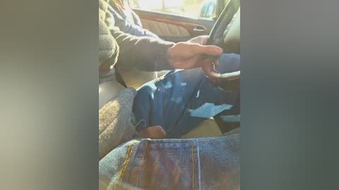 Video of a person driving a car, wearing a gray sweater and blue jeans, with sunlight streaming through the window, highlighting the driver's relaxed posture.