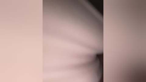 The image is a blurry video featuring a dark-haired person standing in a dimly lit room. The background is indistinct, with soft, muted colors. The person's gender is indeterminate due to the lack of clarity.