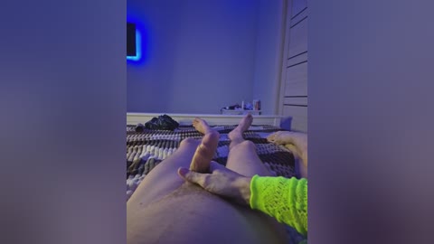 A video captures a person's bare legs and feet, wearing neon green socks, lying on a striped bed in a dimly lit room with blue lighting and a \"1\" sign on the wall.