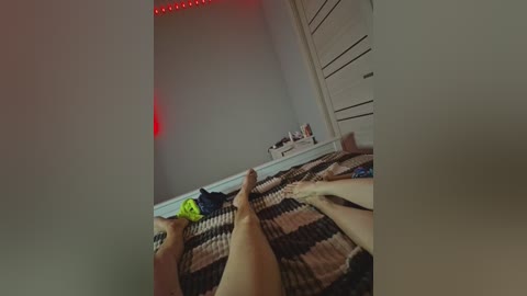 A video shows two pairs of bare legs lying on a striped bedspread, with a green sock visible on one pair. A white dresser and red LED lights on the ceiling are in the background.