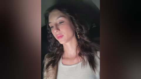 Video of a young woman with long, curly dark hair, wearing a light-colored top and gold hoop earrings, against a dark background.