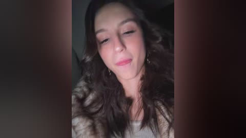 A video of a young woman with long, wavy dark hair, closed eyes, and a serene expression, wearing a light-colored top, with blurred background.