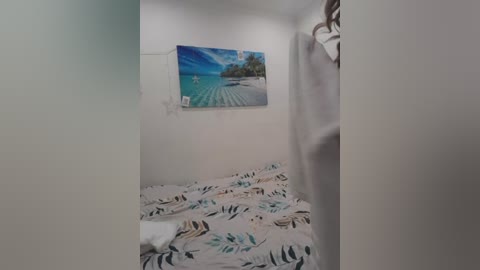 Video of a small, cozy room with a white bed covered in green and beige leaf-patterned sheets, a tropical beach scene painting on the wall, and a white curtain partially drawn.