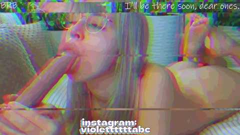 A video shows a topless woman with long blonde hair and glasses, performing oral sex on a large, erect penis. The background is a modern, colorful room. Text reads \"I'll be there soon, clear ones.\