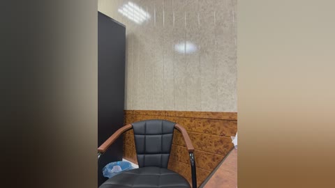 A video of a dimly lit, minimalist office with a black leather chair and wooden armrests, beige wallpaper, and a wooden panel wall. A white light fixture hangs overhead.