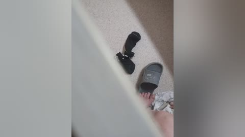 Video of a person's feet in black flip-flops, standing on beige carpet, with a black camera tripod in the background.