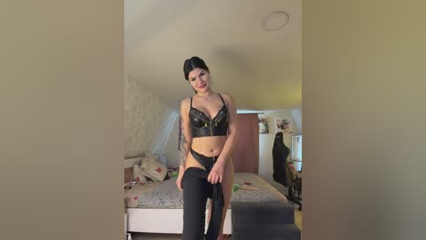 Video of a slender, pale-skinned woman with dark hair, wearing black lace lingerie, standing in a dimly lit, cluttered bedroom.