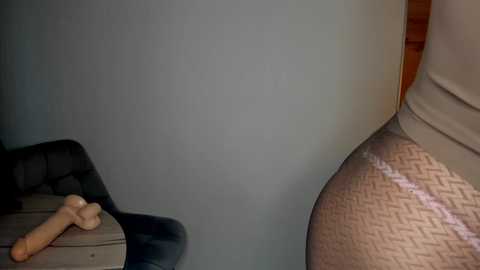 A video depicting a beige chair with a patterned cushion and a wooden cross on a light gray floor. The background is a plain, light blue wall.