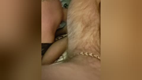 A video showing close-up, intimate view of a person's genital area with pubic hair and a gold chain necklace visible. The background is blurred, focusing on the genital area.