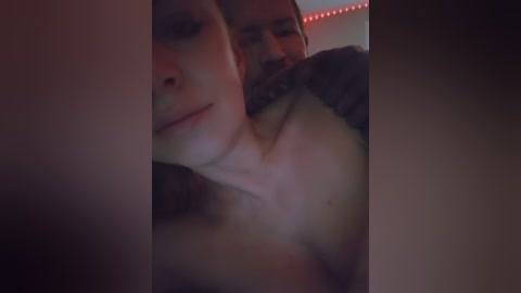 A dimly-lit video captures a close-up of a man's face with short brown hair, wearing a black shirt, gently kissing a woman's neck.