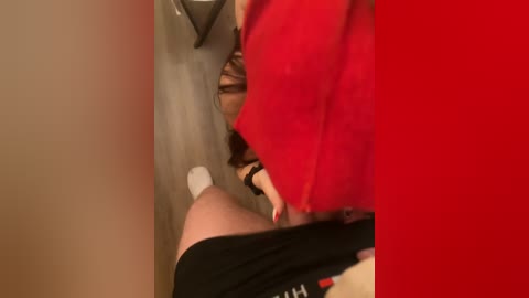 Video of a person in a red shirt, partially visible, peering into a bathroom stall with beige walls and a red divider.