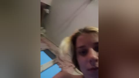 A blurry video of a young woman with blonde hair, seen from the side, standing indoors near a window. The background is indistinct, and the image appears grainy.