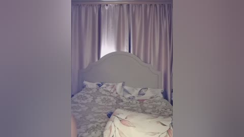 A video of a cozy, dimly lit bedroom featuring a bed with floral bedding, a light-colored headboard, and pastel pink curtains. The room exudes a soft, nostalgic atmosphere.