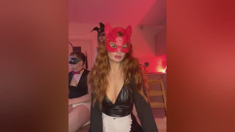 Video of a woman in a red Catwoman mask, black leather top, and white skirt, standing in a dimly lit room with red lighting.