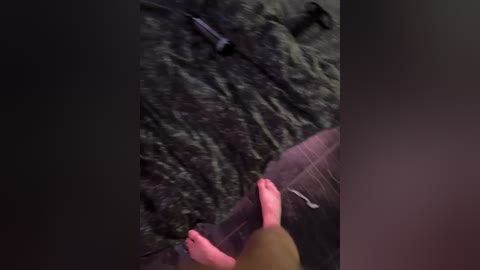 A video captures a person's hand with pink nails holding a metal rod, standing on a dark, textured carpet with scattered tools, including a hammer, on the floor. The image is slightly blurred, giving a grainy, amateurish appearance.