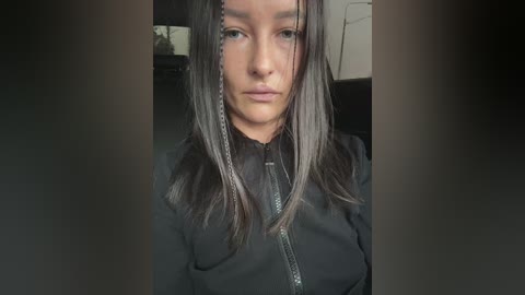 Video of a young woman with straight, dark brown hair, wearing a black jacket, looking serious and slightly out of focus.