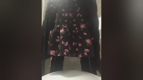 Video of a person in a black floral dress with pink flowers, standing in a dimly lit bathroom with a white toilet visible in the foreground.