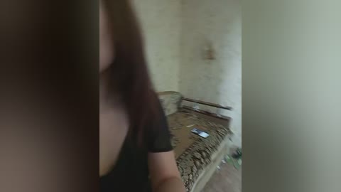 A blurred, low-resolution video captures a woman with long brown hair, wearing a black top, sitting on a dilapidated couch in a dimly lit, rundown room. The background features peeling walls and scattered debris.