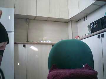 Video of a modern, compact kitchen with light wood cabinets, a teal chair, a maroon cushion, a black microwave, and a white fridge, showcasing a minimalist and functional design.