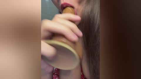 A close-up video of a woman with light skin, long brown hair, and red lipstick, holding a wooden spoon to her mouth, wearing a red-patterned dress.