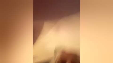 A blurred video of a person's legs and feet in light-colored socks, partially obscured by a beige curtain. The image is soft-focused, with a warm, muted color palette.