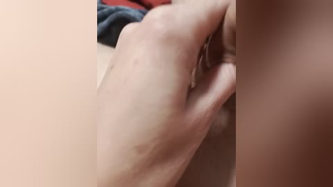 A close-up video of a fair-skinned hand with visible stretch marks on the forearm. The background is blurred, showing a person in a red shirt.