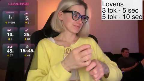 A video shows a blonde woman with glasses and a yellow cardigan, seated in a dark room, watching a monitor displaying \"Loveense\" and \"Lovens 3 tok-5 sec-10 sec.\