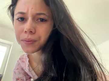 Video of a young woman with long, straight black hair and light skin, wearing a pink floral shirt, making a pouty face. Background shows a white wall and part of a window.