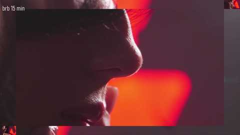 A close-up, grainy video of a person's profile, illuminated by a red light, with the words \"brt 15 min\" overlaid. The background is blurred and dark.