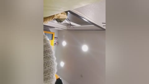 Video of a small, cozy attic bedroom with a slanted ceiling, a large, fluffy white comforter, and a yellow wall. Three bright white lights illuminate the room, creating a warm, inviting atmosphere.