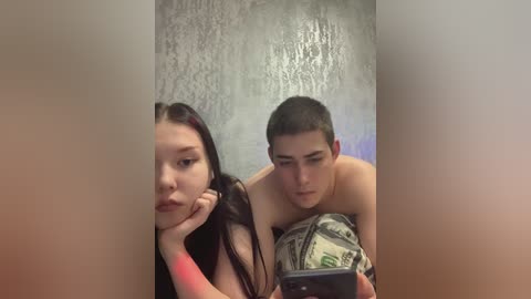 A video shows a shirtless young man with short hair and a woman with long dark hair, both using a mirror to check their reflection.