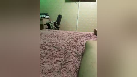 Video of a dimly lit bedroom with a soft pink shag rug, a beige wall, and a black office chair positioned next to a cluttered desk.