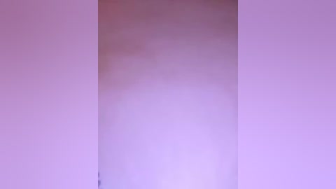 Video of a blurry, light purple wall with a faint, indistinct figure possibly standing in the corner. The image has a soft focus and minimal contrast, creating an ethereal, dreamlike atmosphere.